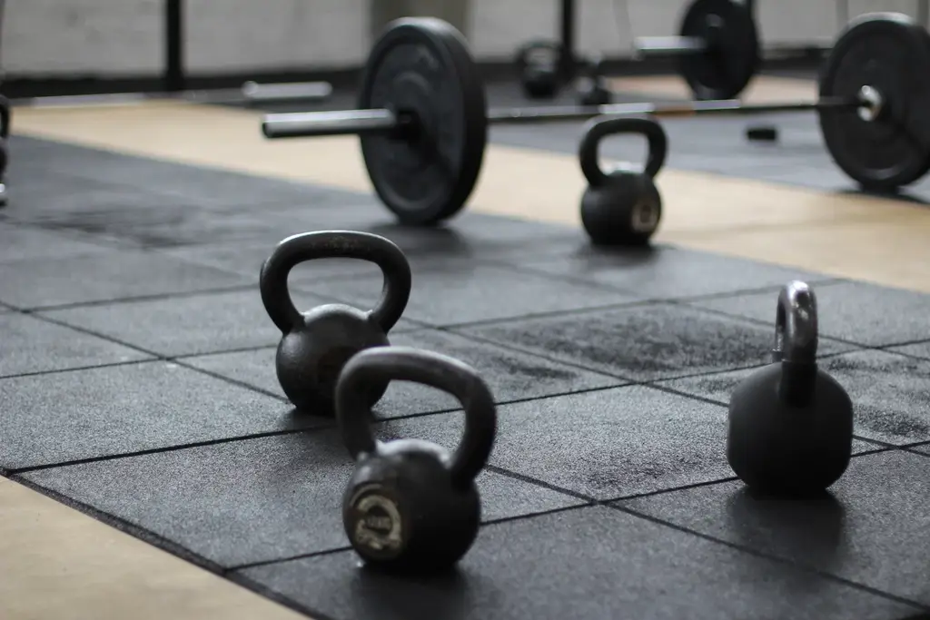 Kettlebells and barbells scattered on a rubber gym floor