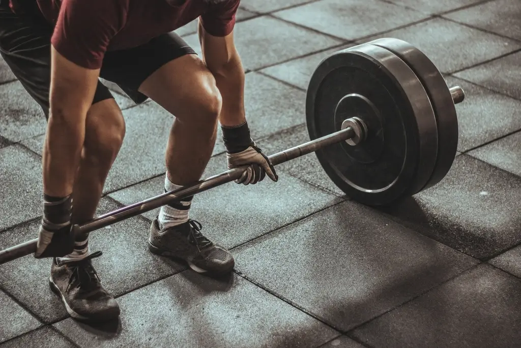A lifter in a hip hinge gripping a loaded barbell on rubber flooring