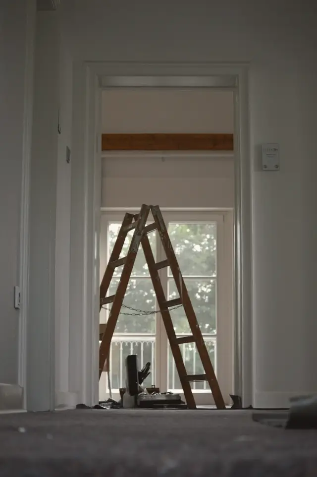 A wooden stepladder standing in a bright, freshly patched hallway of an older house