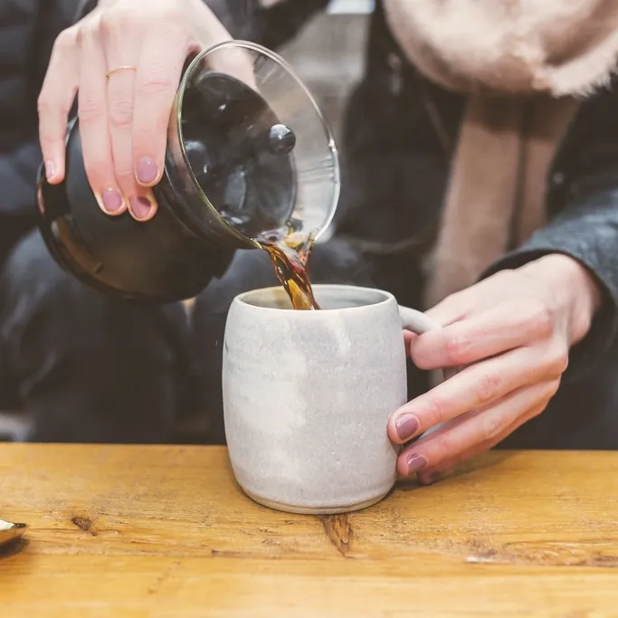 Coffee being poured from a glass carafe into a stoneware mug