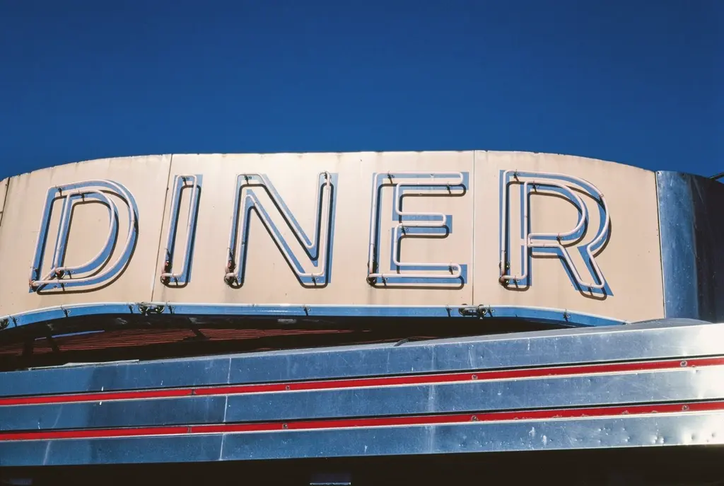 A retro neon outline DINER sign against a blue sky